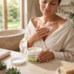 Woman in a bathrobe applying Bienenprodukte Shop Aloe Vera and Royal Jelly soft body cream to her chest in a bathroom.