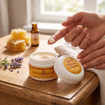 Bienenprodukte Shop API Honig Creme mit Jojobaöl auf einem Finger, präsentiert neben Honigwaben und Lavendel.